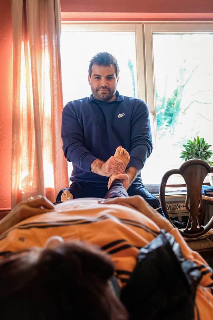 Mobiler Physiotherapeut aus Hamburg behandelt das Bein eines Patienten auf einer Behandlungsliege