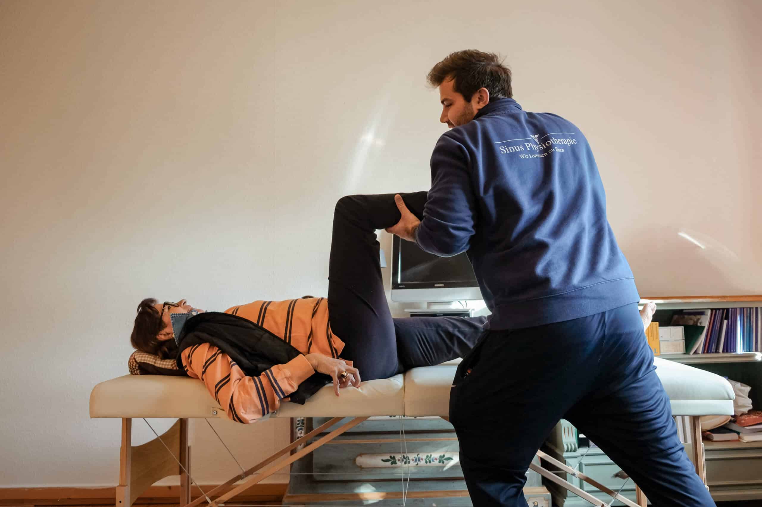 Mobiler Physiotherapeut aus Hamburg mobilisiert das Bein einer Patientin auf einer Behandlungsliege