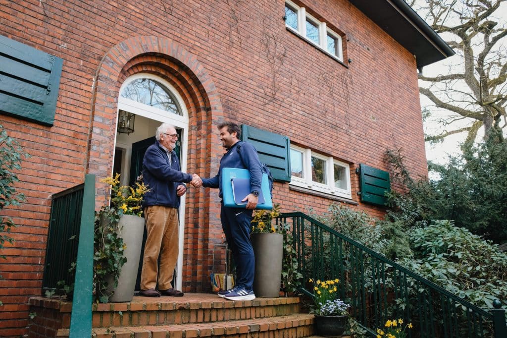 Mobiler Physiotherapeut aus Hamburg trifft einen Patienten vor einem Wohnhaus zum Hausbesuch