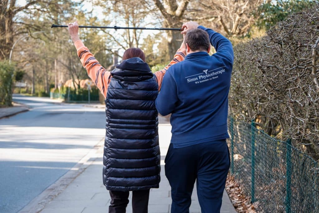 Physiotherapeut begleitet eine Patientin bei einer Gehübung im Freien zur Förderung der Beweglichkeit