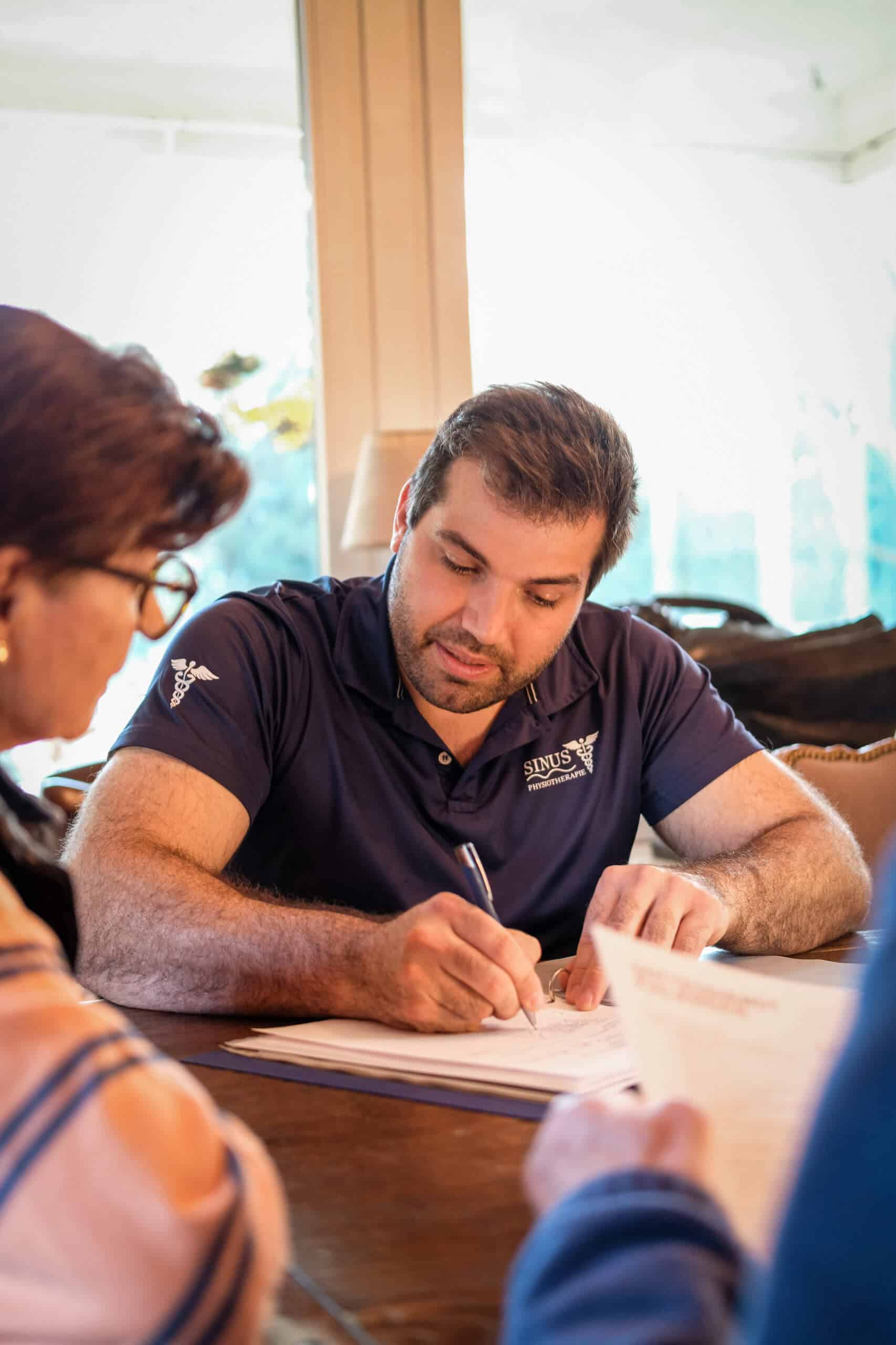 Physiotherapeut bespricht einen Therapieplan mit einer Patientin und macht sich Notizen